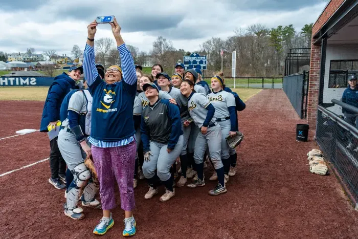 莎拉Willie-LeBreton takes a selfie with the softball team behind her.